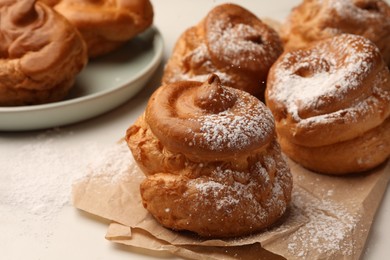 Photo of Delicious profiteroles with powdered sugar on parchment paper, closeup