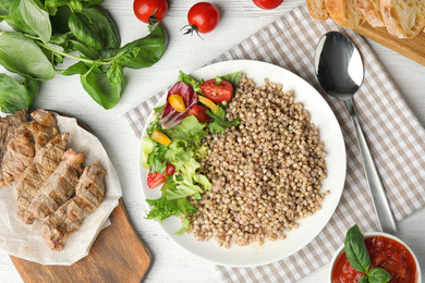 Photo of Tasty buckwheat porridge with salad on white wooden table, flat lay