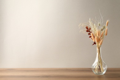 Photo of Dried flowers in vase on table against light background. Space for text