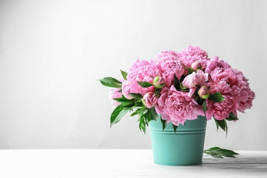 Bucket with beautiful peony flowers on table against light background