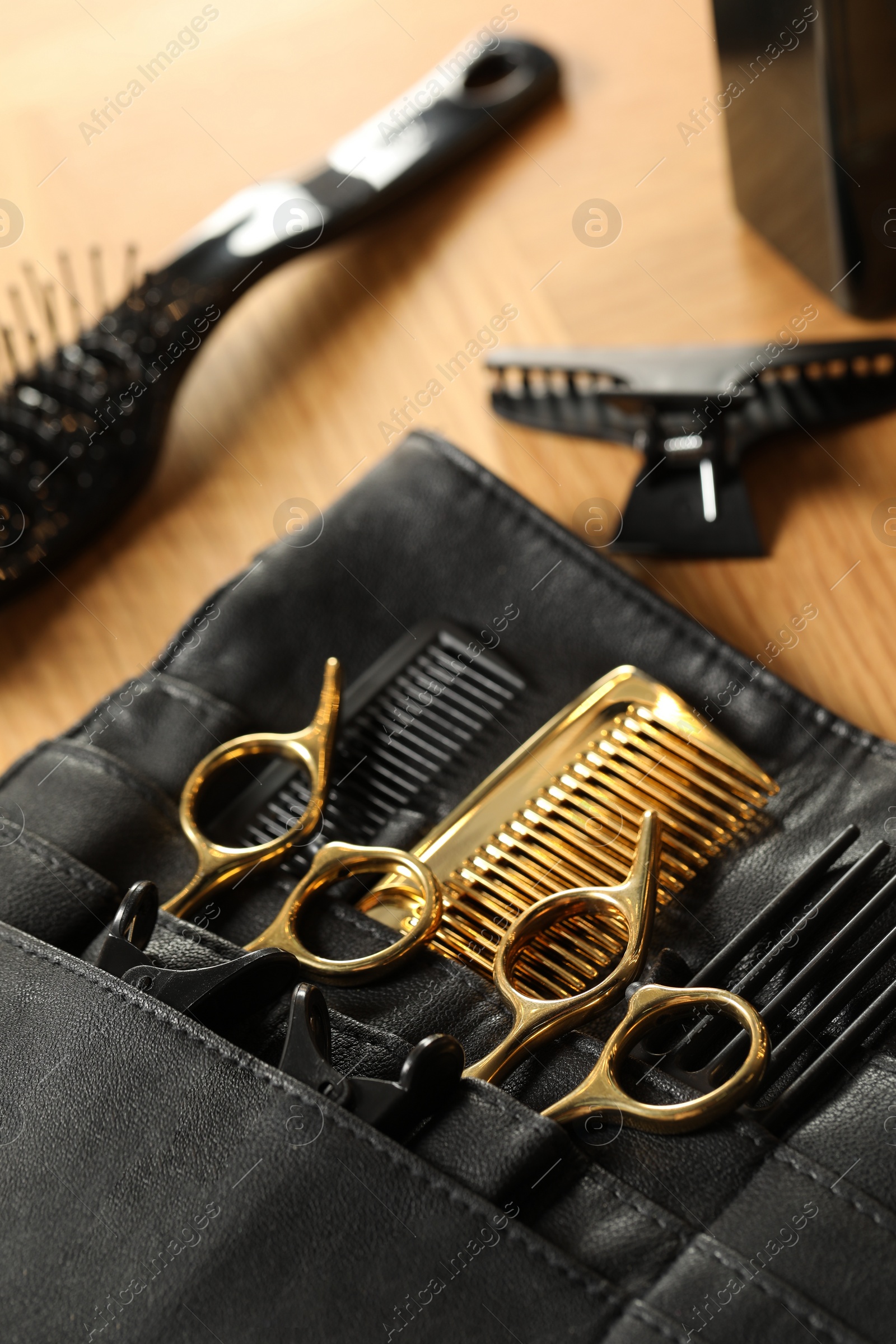 Photo of Hairdresser tools. Professional scissors and combs in leather organizer on wooden table, closeup