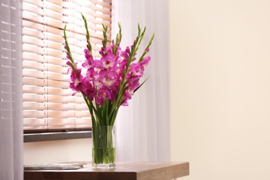 Vase with beautiful pink gladiolus flowers on wooden table in room, space for text