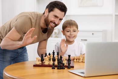 Photo of Father and son learning to play chess with online tutor indoors