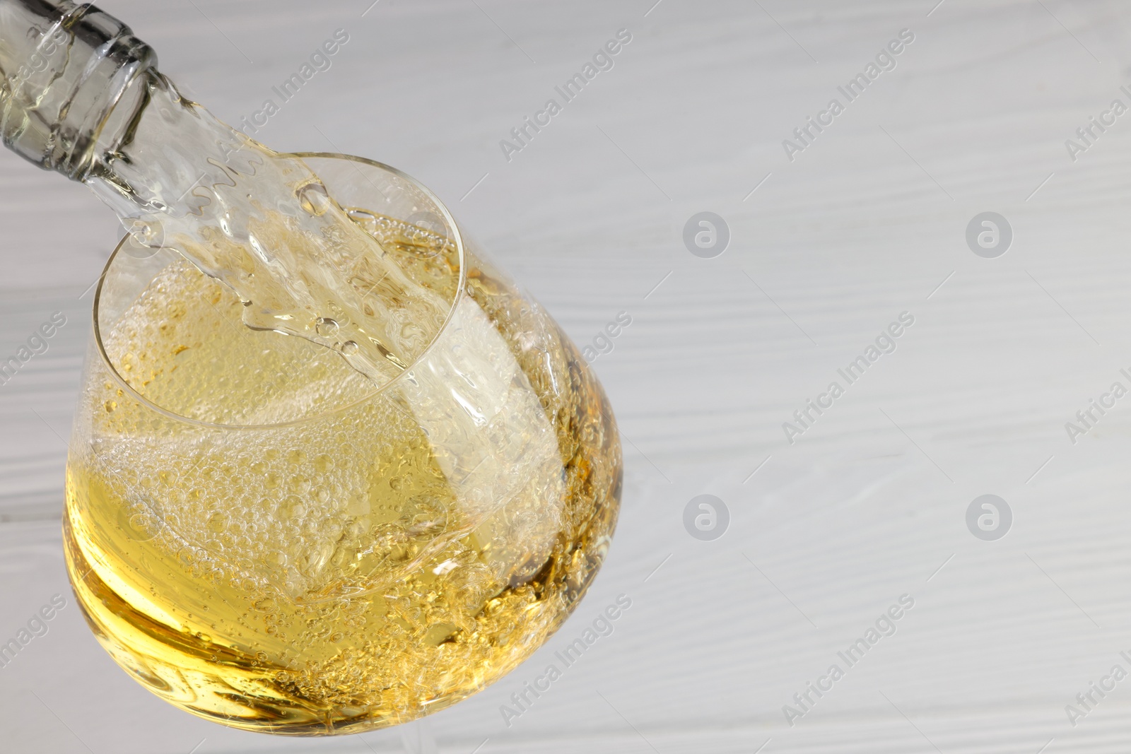 Photo of Pouring tasty aromatic wine in glass at white wooden table, closeup. Space for text