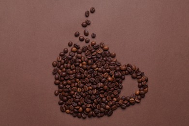 Cup made of coffee beans on brown background, top view