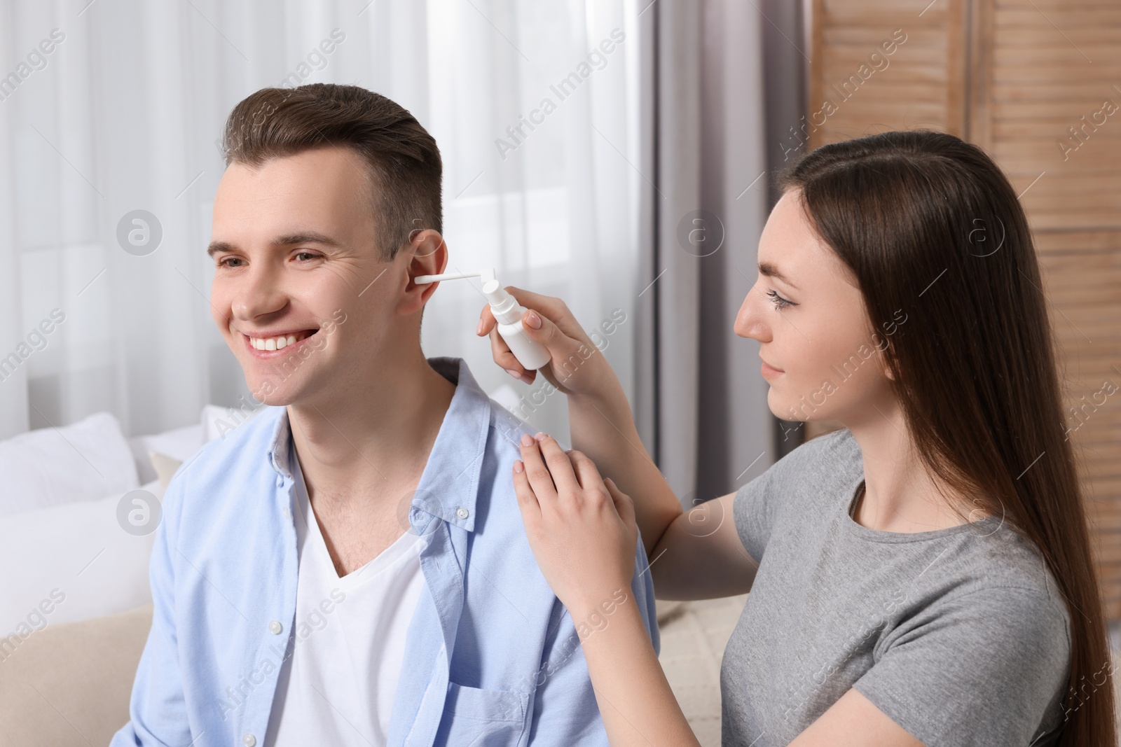Photo of Woman spraying medication into man's ear at home