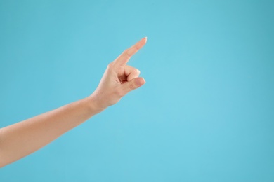 Photo of Closeup view of woman pointing at something on light blue background, space for text. Finger gesture