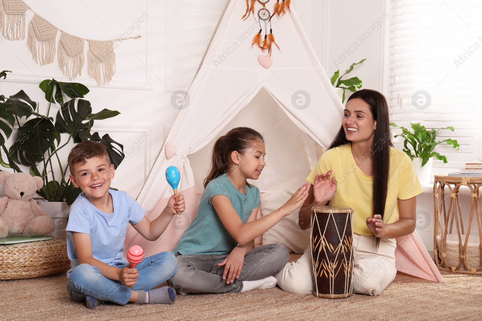 Photo of Mother and children playing near toy wigwam at home