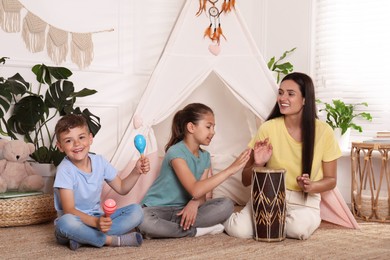Mother and children playing near toy wigwam at home