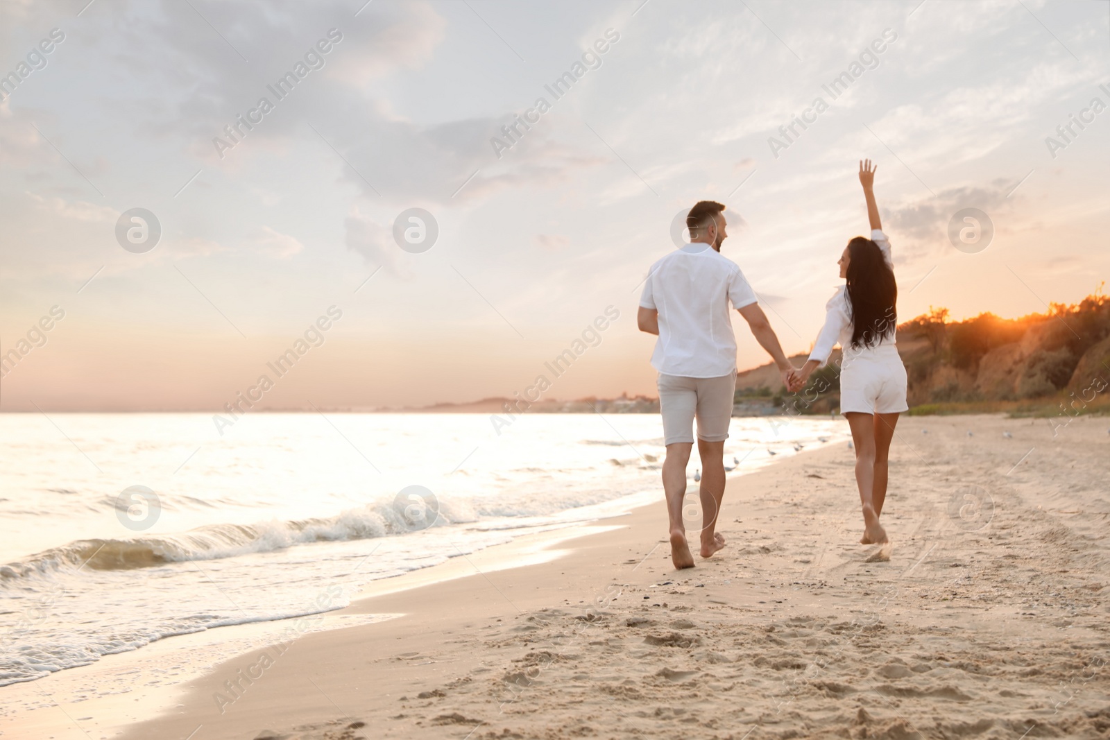 Photo of Lovely couple running together on beach at sunset, back view