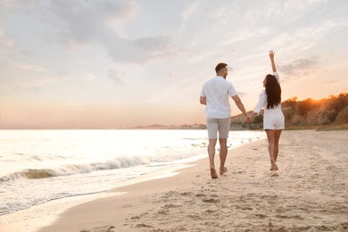 Photo of Lovely couple running together on beach at sunset, back view