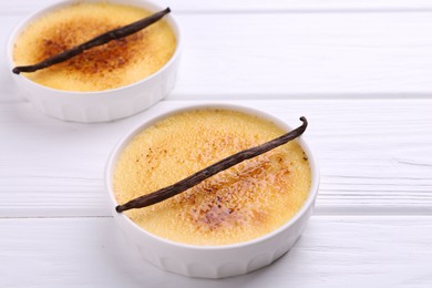 Photo of Delicious creme brulee in bowls and vanilla pods on white wooden table