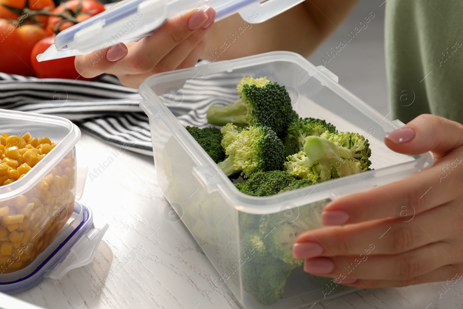 Photo of Woman closing plastic container with lid at white wooden table, closeup. Food storage