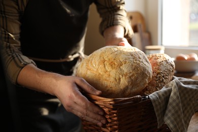 Photo of Man holding wicker basket with different types of bread indoors, closeup