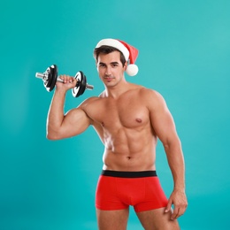 Sexy shirtless Santa Claus with dumbbell on blue background