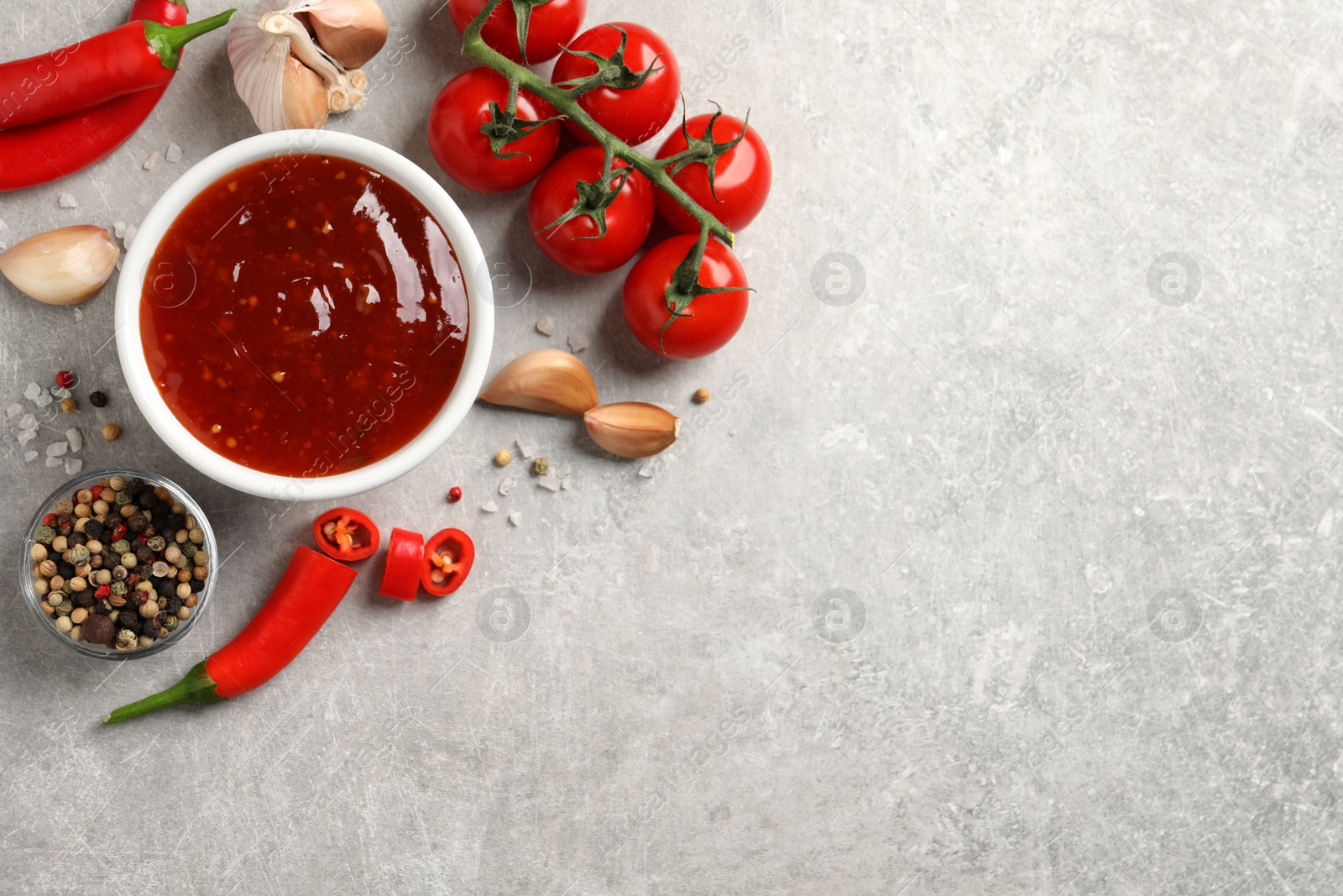 Photo of Spicy chili sauce and ingredients on light grey table, flat lay. Space for text