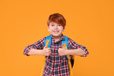 Photo of Happy schoolboy showing thumbs up on orange background