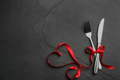 Photo of Cutlery set and red ribbon on black background, flat lay with space for text. Valentine's Day dinner