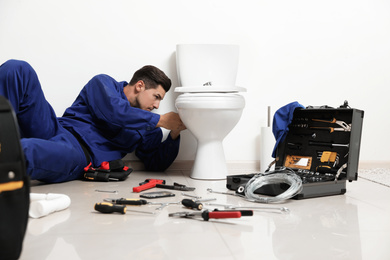 Professional plumber working with toilet bowl in bathroom