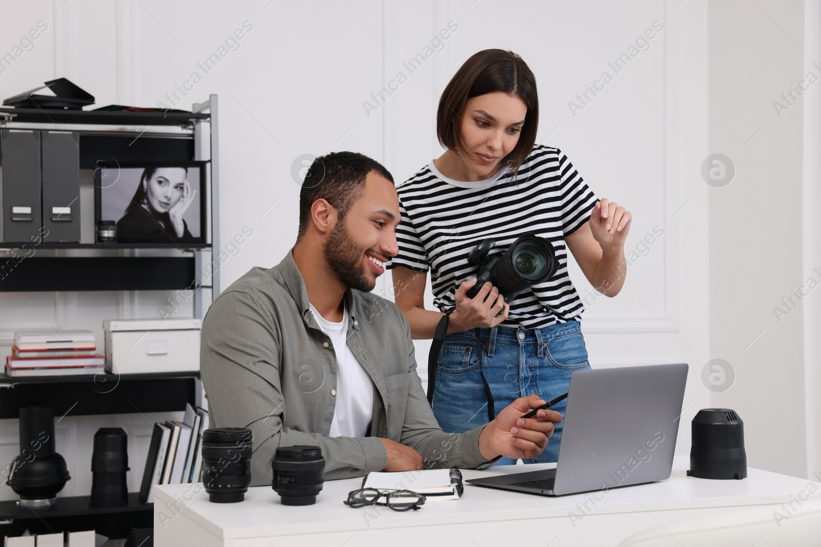 Photo of Young professional photographers with camera working on laptop in modern photo studio