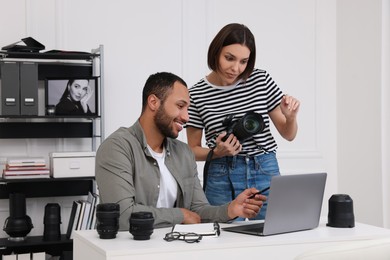Photo of Young professional photographers with camera working on laptop in modern photo studio