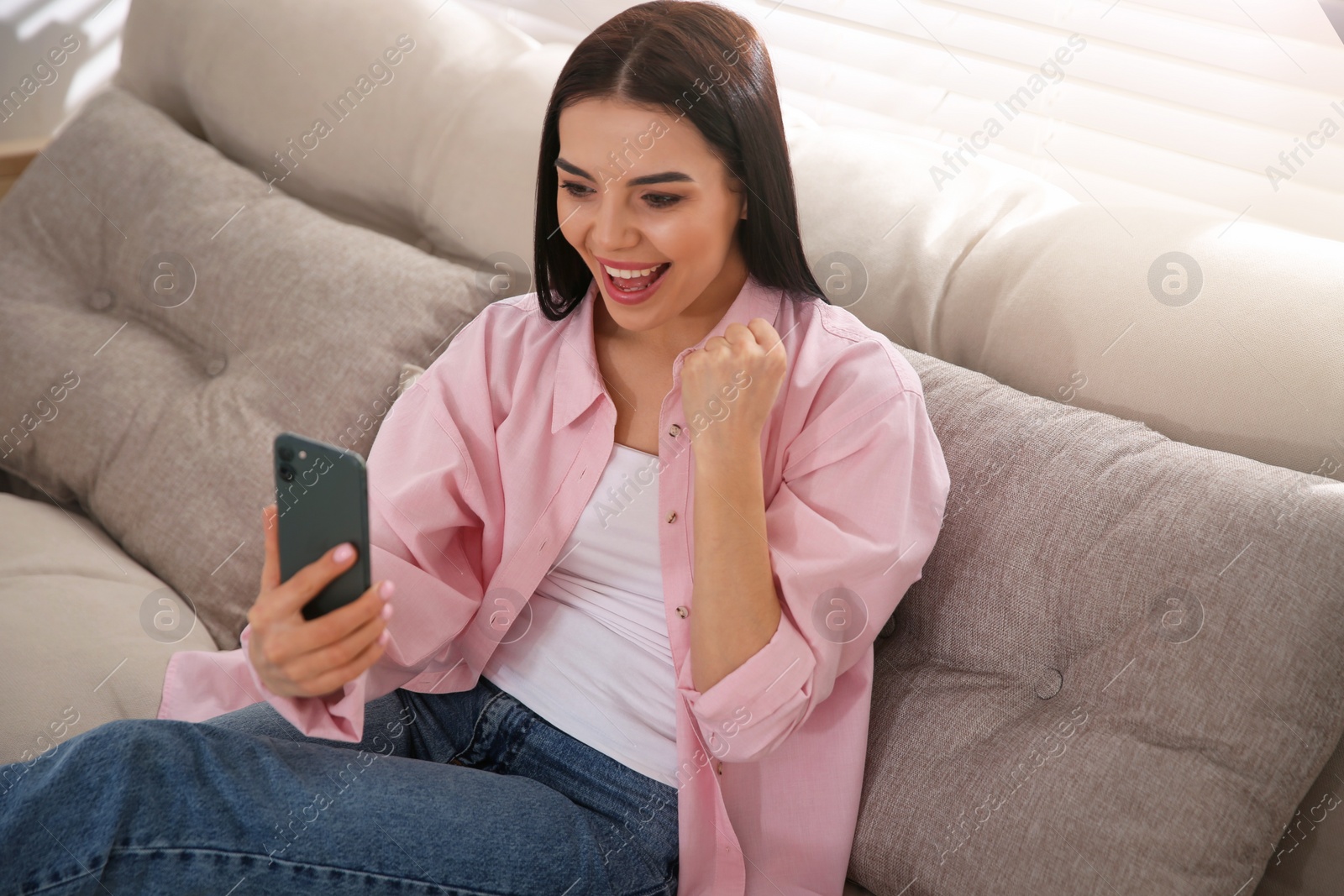 Photo of Emotional woman participating in online auction using smartphone at home