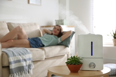 Modern air humidifier and blurred woman resting on background