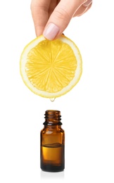 Photo of Woman holding slice of lemon above bottle with essential oil on white background