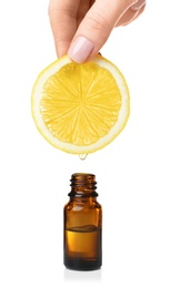 Woman holding slice of lemon above bottle with essential oil on white background