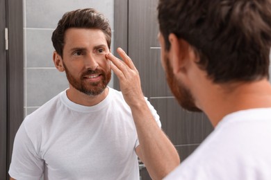 Photo of Handsome bearded man looking at mirror in bathroom