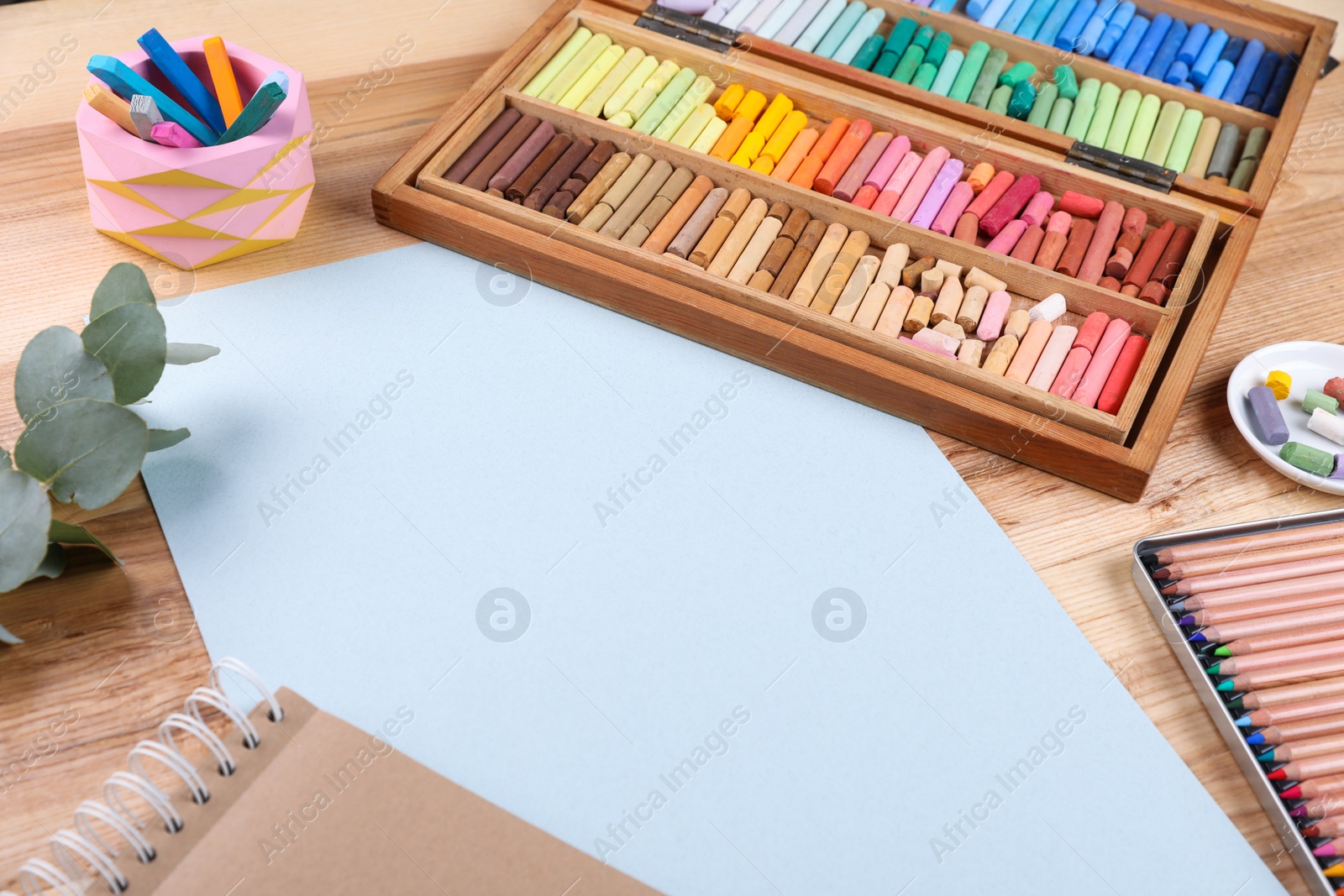 Photo of Blank paper, soft pastels and drawing pencils on wooden table at artist's workplace. Space for design