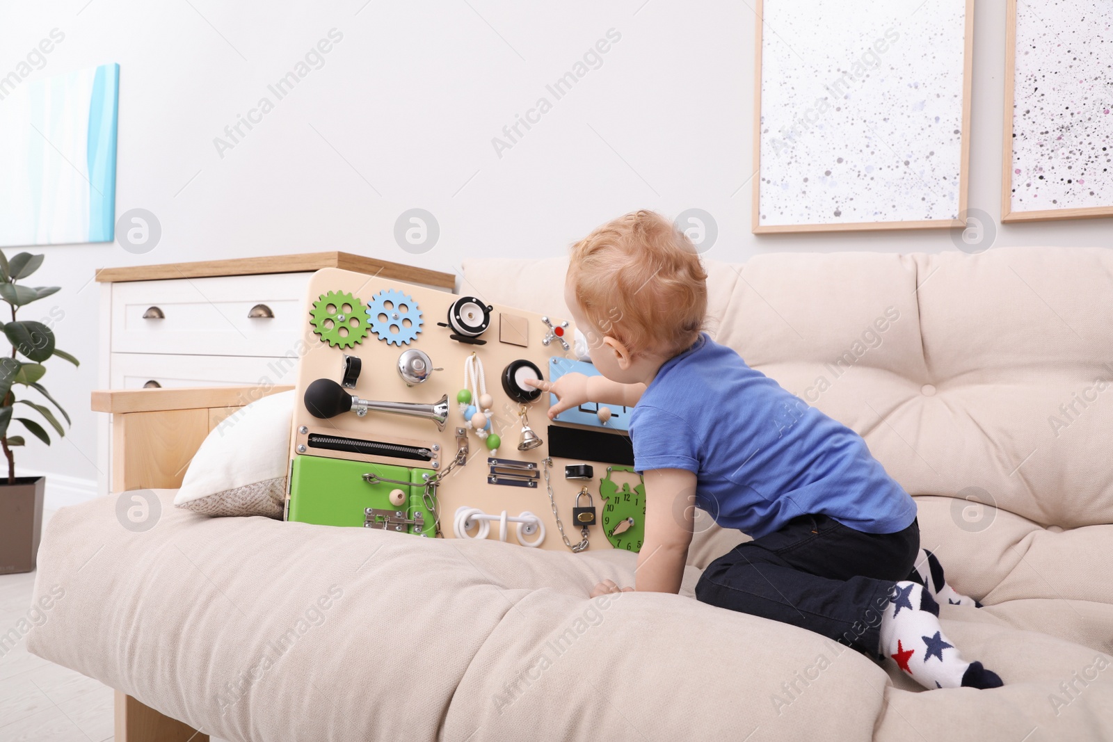 Photo of Cute little boy playing with busy board on sofa at home