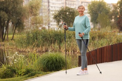 Photo of Senior woman performing Nordic walking outdoors, space for text