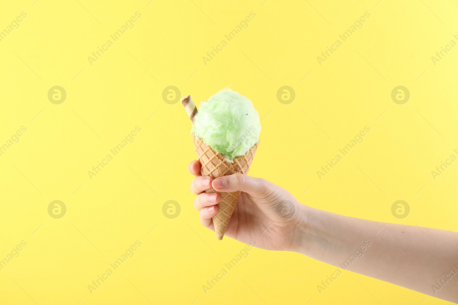 Photo of Woman holding waffle cone with cotton candy on yellow background, closeup