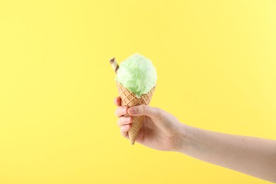 Woman holding waffle cone with cotton candy on yellow background, closeup