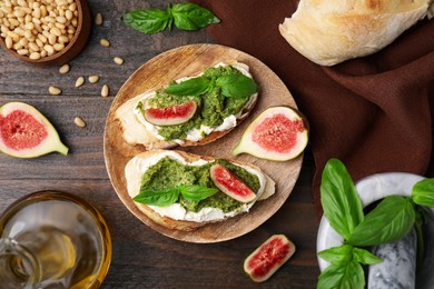 Photo of Tasty bruschettas with cream cheese, pesto sauce, figs and fresh basil on wooden table, flat lay