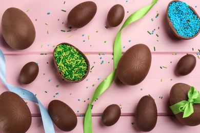 Photo of Sweet chocolate eggs and sprinkles on pink wooden table, flat lay