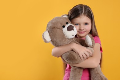 Photo of Cute little girl with teddy bear on yellow background. Space for text