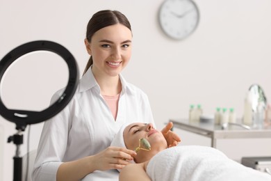 Photo of Cosmetologist making face massage with roller to client in clinic