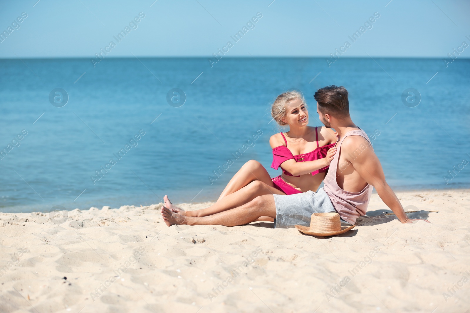 Photo of Happy young couple sitting together at beach on sunny day