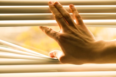 Photo of Man separating slats of white blinds indoors, closeup