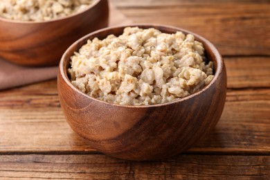 Tasty boiled oatmeal in bowl on wooden table, closeup