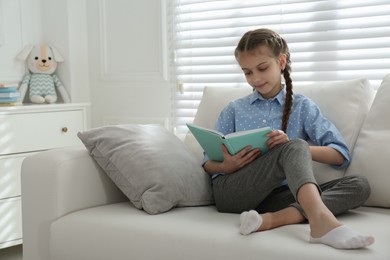 Photo of Cute little girl reading book on sofa at home