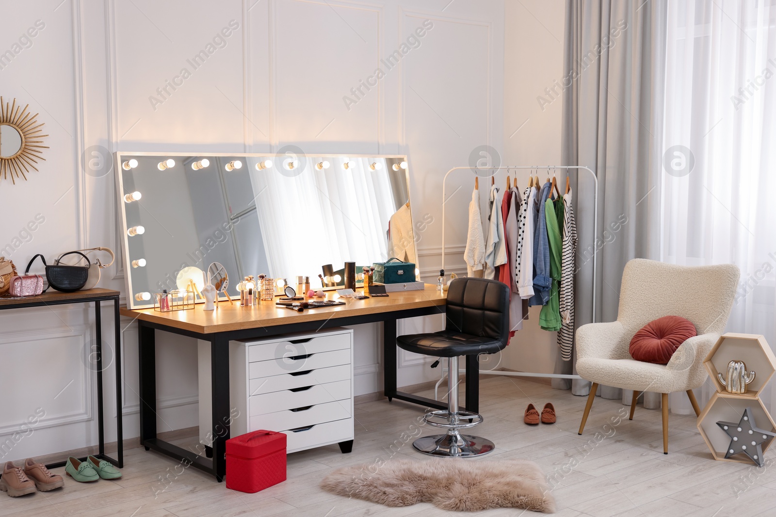 Photo of Makeup room. Stylish dressing table with mirror, chair and clothes rack