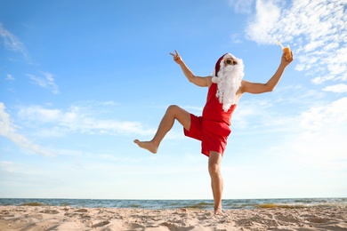 Photo of Santa Claus with cocktail having fun on beach, space for text. Christmas vacation