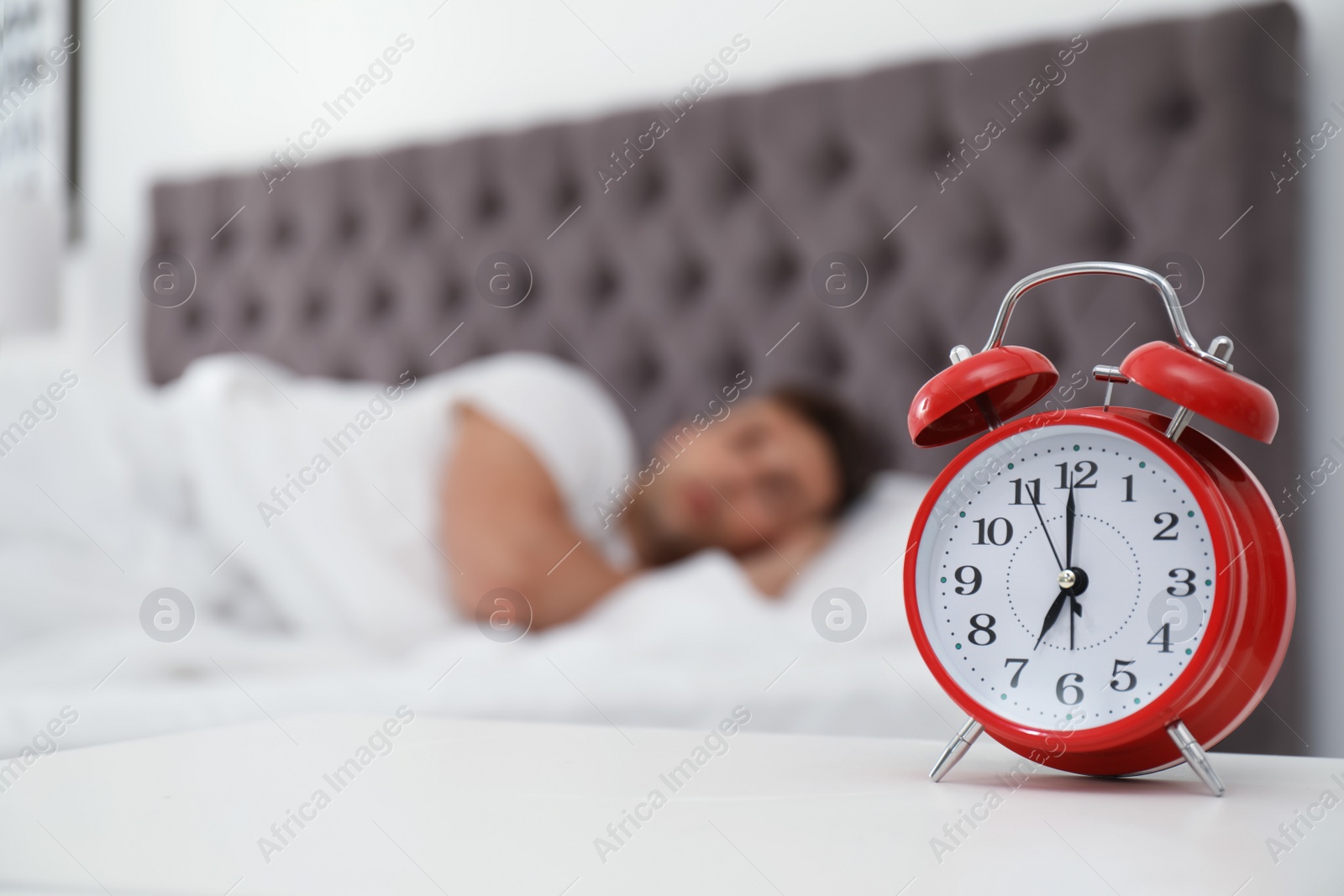 Photo of Analog alarm clock and blurred man on background. Time of day