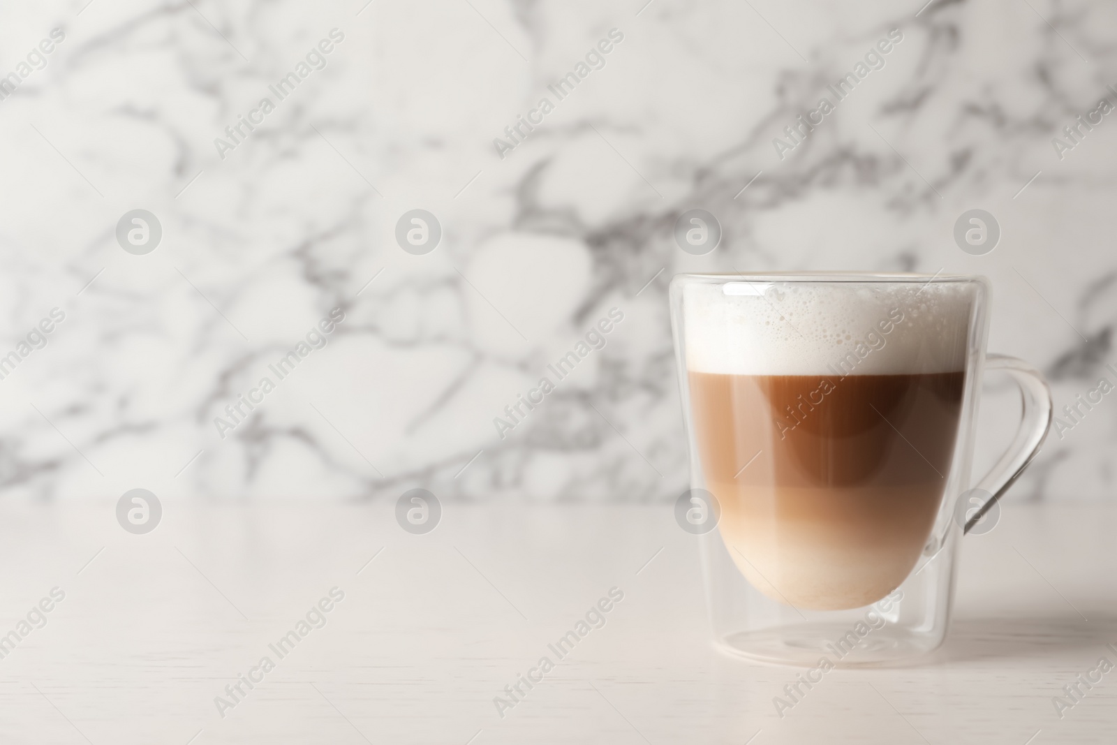 Photo of Glass cup of delicious layered coffee on white table against marble background, space for text