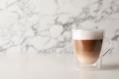 Glass cup of delicious layered coffee on white table against marble background, space for text