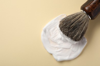 Brush with shaving foam on beige background, top view. Space for text