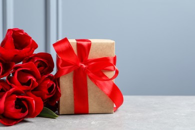 Photo of Beautiful gift box with bow and red tulip flowers on light table, space for text